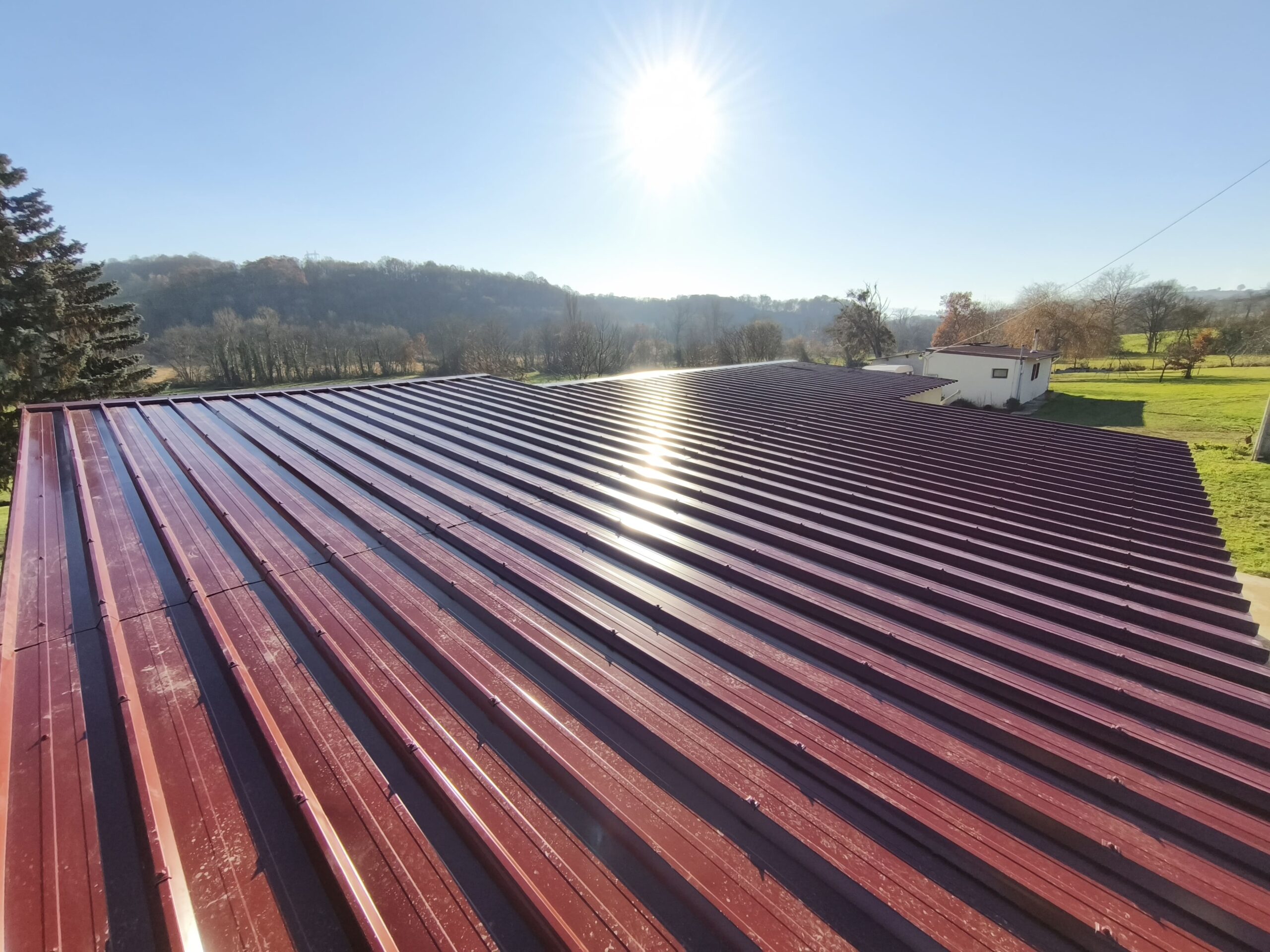 Toiture en tôle rouge rénovée par dkz avec vue sur paysage rural des hautes-pyrénées sous ciel bleu
